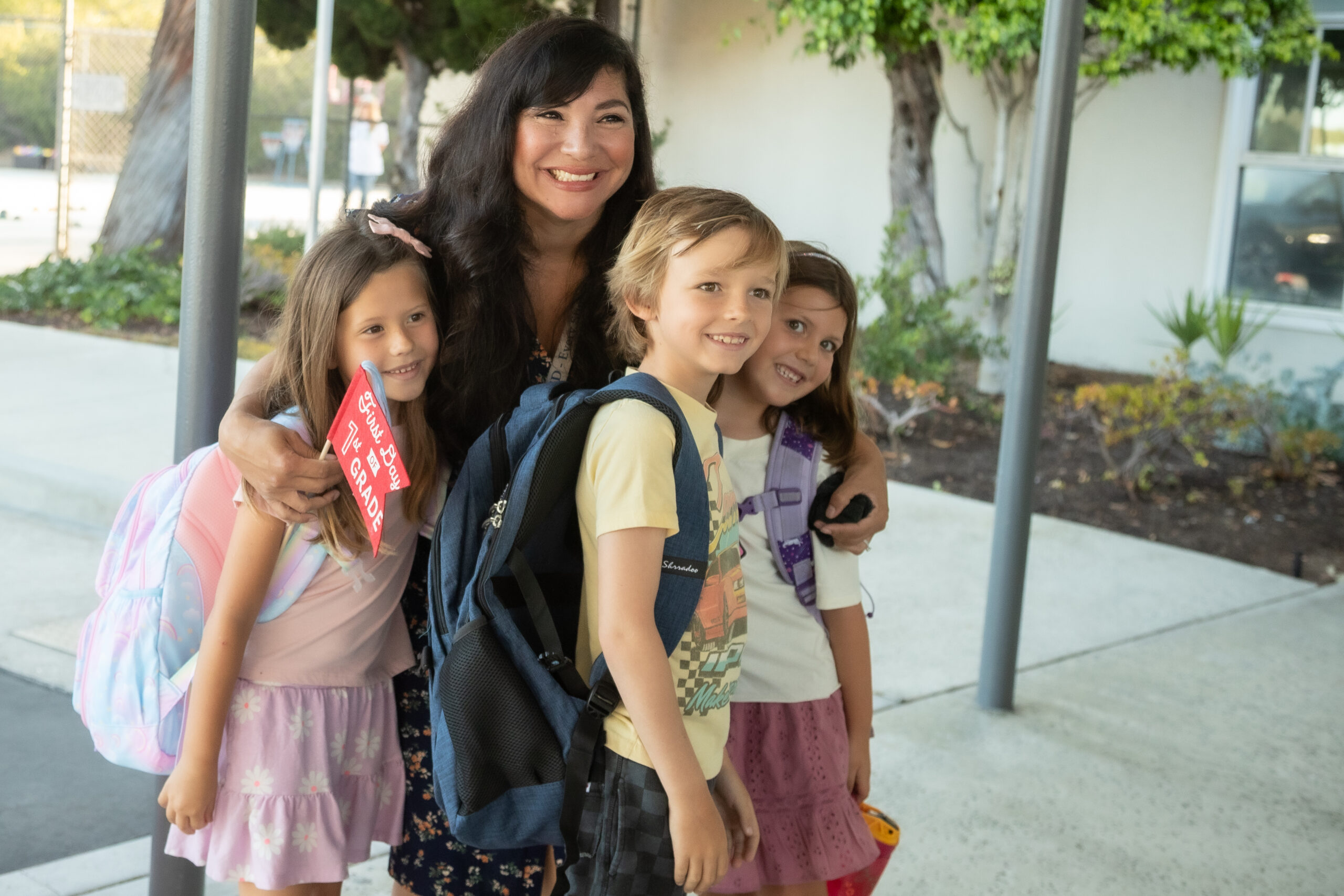 An adult poses with three elementary school students wearing backpacks as they arrive for the first day of school at a Laguna Beach Unified School District elementary campus.