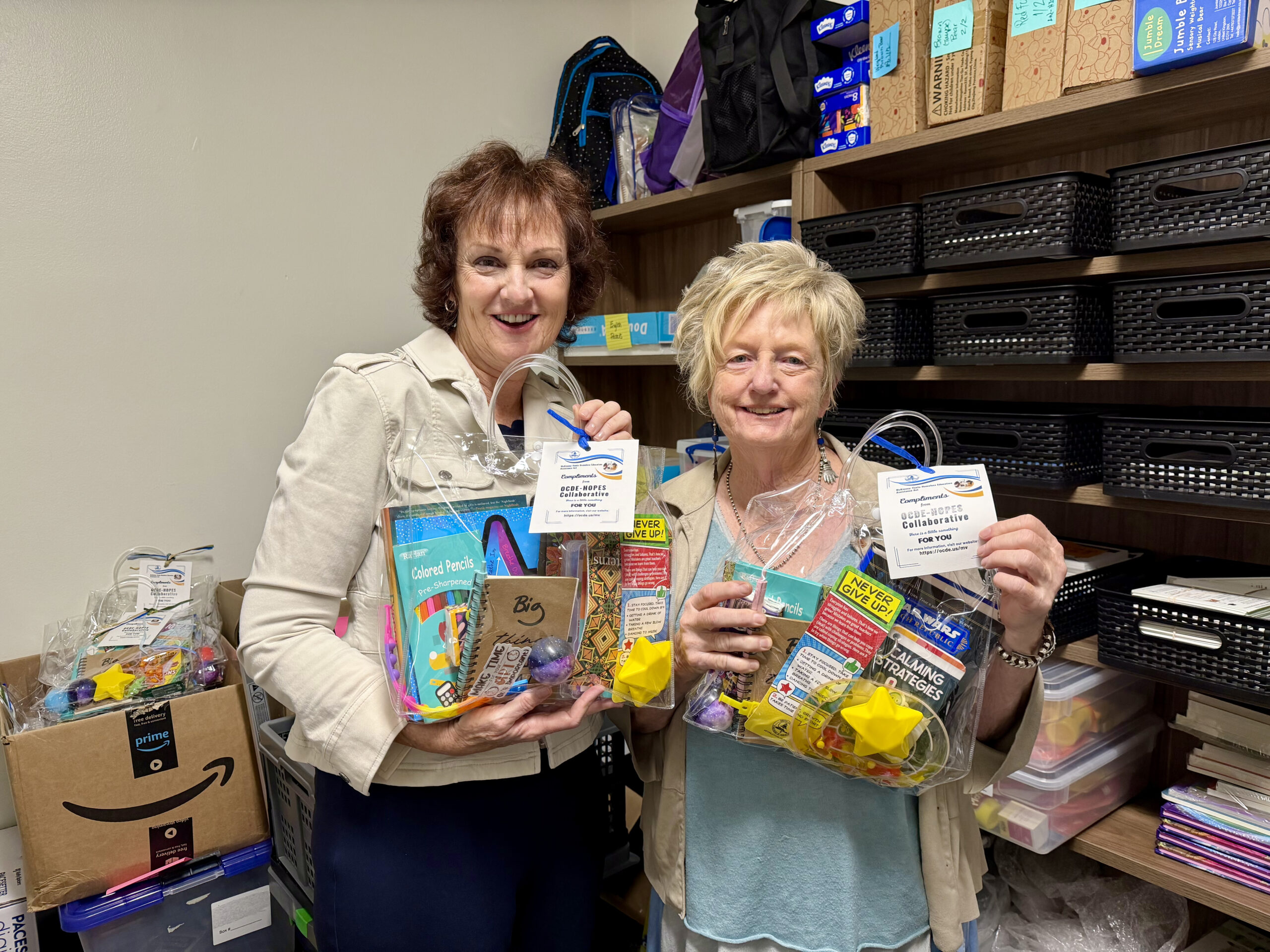 OCDE Student Programs and Services Coordinator Jeanne Awrey, left, and Senior Administrative Assistant Terri Glover hold welcome gifts prepared for children and youth staying in local homeless shelters. The gifts include school supplies, books and other items selected for students of different ages.