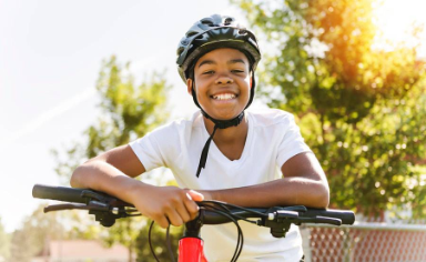 Young person wearing a helmet smiles while sitting on an e-bike outdoors.