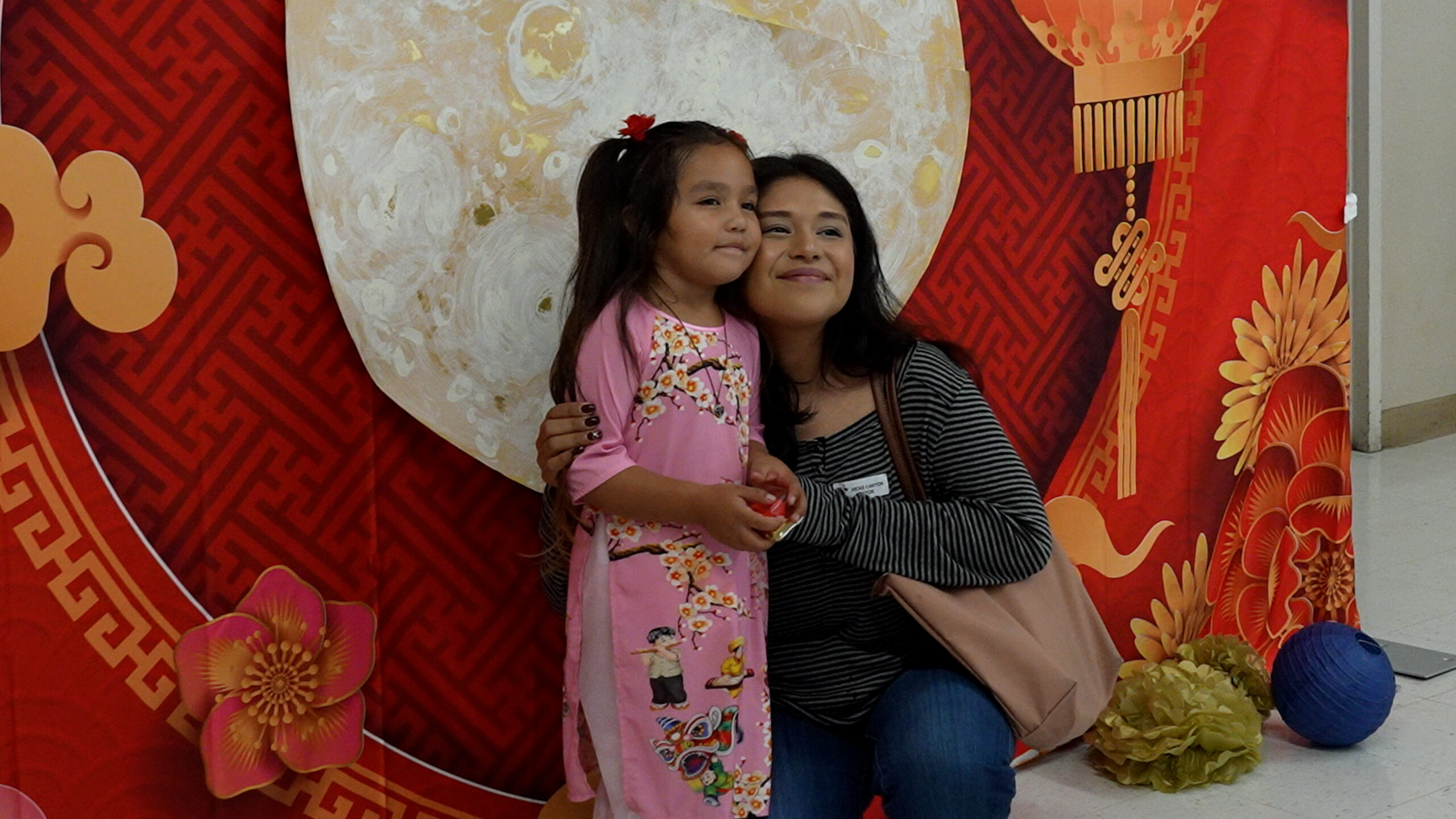 A child poses for a photo with a family member in front of a festive moon-themed backdrop during the Mid-Autumn Festival celebration at Hicks Canyon Elementary School in Tustin. (Photo courtesy of the Tustin Unified School District)