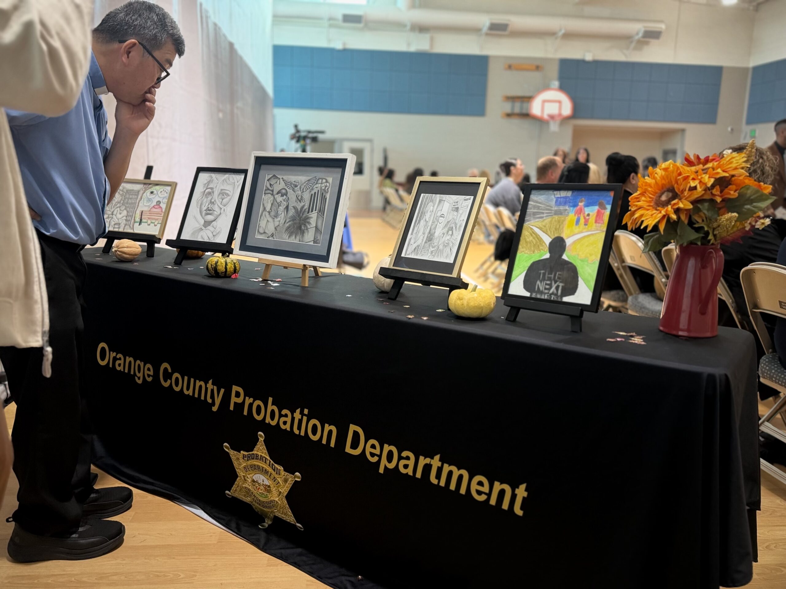 Onlookers examine the five winning drawings at the Ninth Annual Essay and Visual Arts Contest for incarcerated youth at Otto A. Fischer School within Orange County Juvenile Hall.