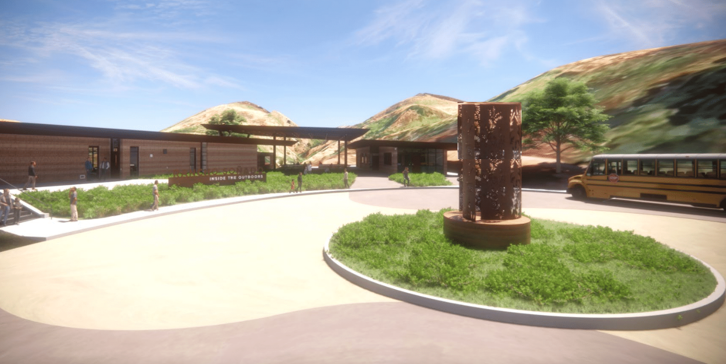Architectural rendering of the future Rancho Soñado Inside the Outdoors Education Center, showing low-profile buildings, landscaped walkways, a circular entry area and a school bus, with hills in the background.