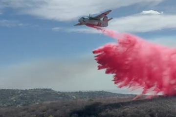 A firefighting aircraft releases a large plume of bright pink fire retardant over brush-covered hills during the Norte Fire in southern Orange County.