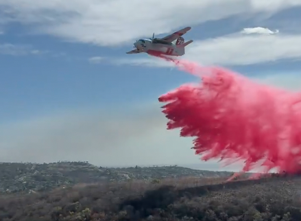 A firefighting aircraft releases a large plume of bright pink fire retardant over brush-covered hills during the Norte Fire in southern Orange County.