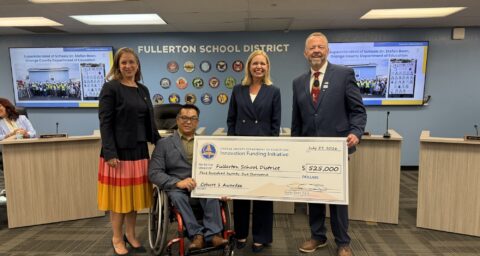 Four education leaders pose at the Fullerton School District Board of Education meeting on July 27, 2026, holding a large ceremonial $525,000 check from OCDE’s Innovation Funding Initiative.