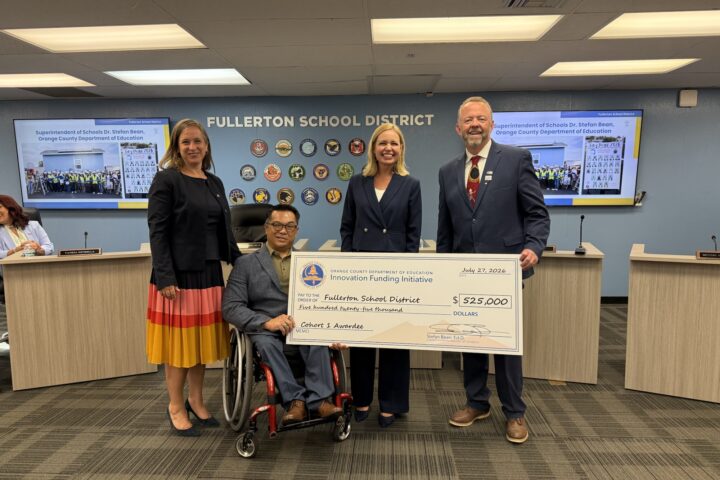 Four education leaders pose at the Fullerton School District Board of Education meeting on July 27, 2026, holding a large ceremonial $525,000 check from OCDE’s Innovation Funding Initiative.